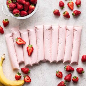 Strawberry banana gogurts lined up with strawberries and bananas around them.