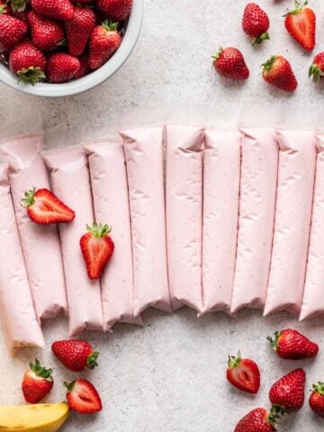 Strawberry banana gogurts lined up with strawberries and bananas around them.