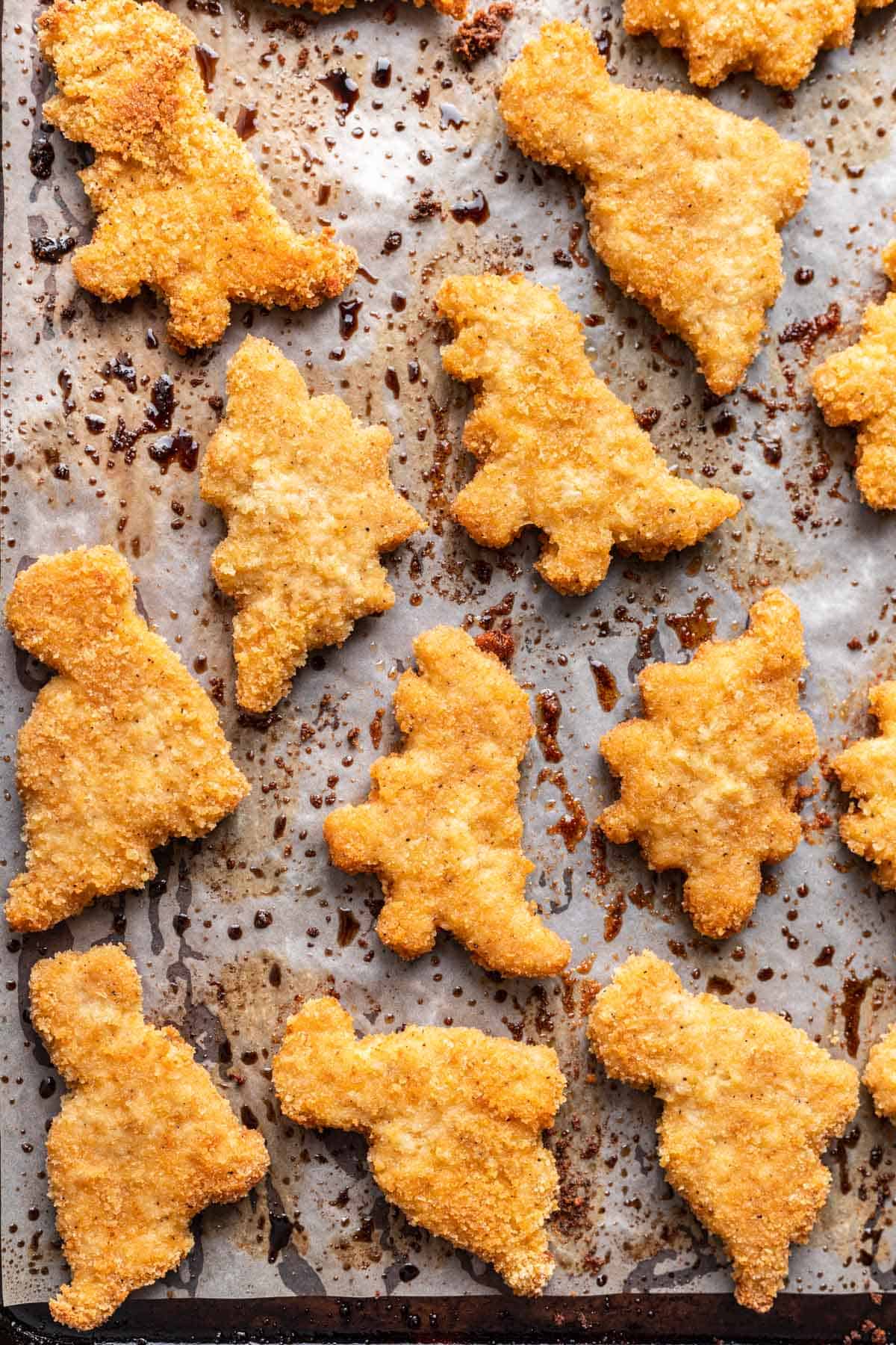 Golden brown dinosaur chicken nuggets on a baking sheet, fresh from the oven.