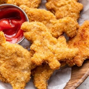 Golden brown dinosaur chicken nuggets stacked on a plate.