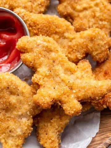 Golden brown dinosaur chicken nuggets stacked on a plate.