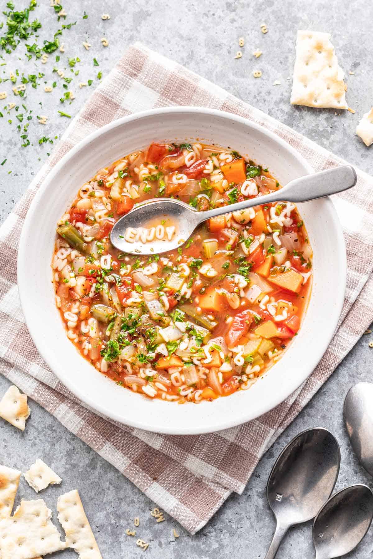Homemade alphabet soup in a white bowl, served with crackers on the side.