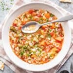 Alphabet soup in a white bowl with a spoon, spelling "ENJOY" with the ABC pasta.