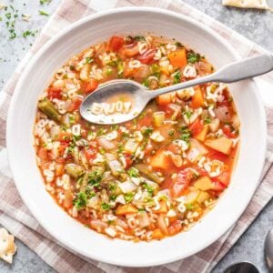 Alphabet soup in a white bowl with a spoon, spelling "ENJOY" with the ABC pasta.
