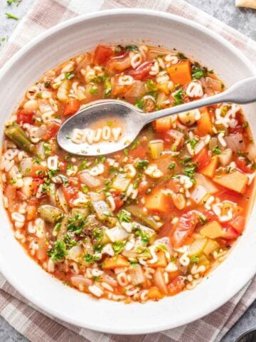 Alphabet soup in a white bowl with a spoon, spelling "ENJOY" with the ABC pasta.
