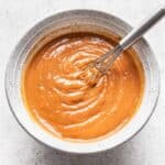 Spicy peanut sauce in a white bowl with a small whisk.