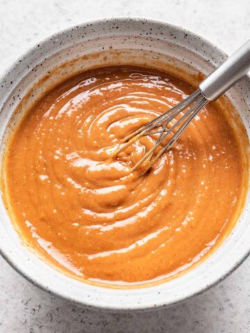 Spicy peanut sauce in a white bowl with a small whisk.