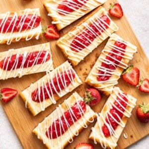Copycat Philadelphia Cheesecake Bars on a wood cutting board with strawberries.