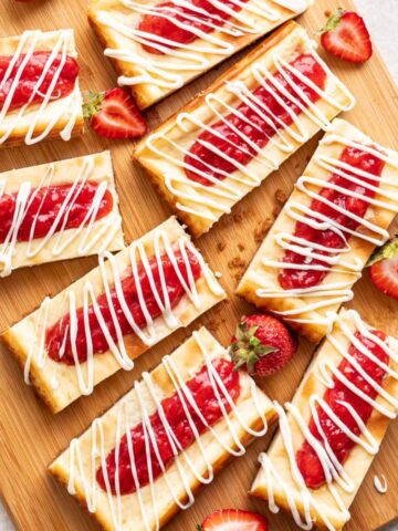 Copycat Philadelphia Cheesecake Bars on a wood cutting board with strawberries.