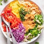 Assorted veggies on top of cooked pasta with peanut sauce on top.