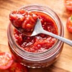 Tomato jam on a spoon resting on top of a jar.