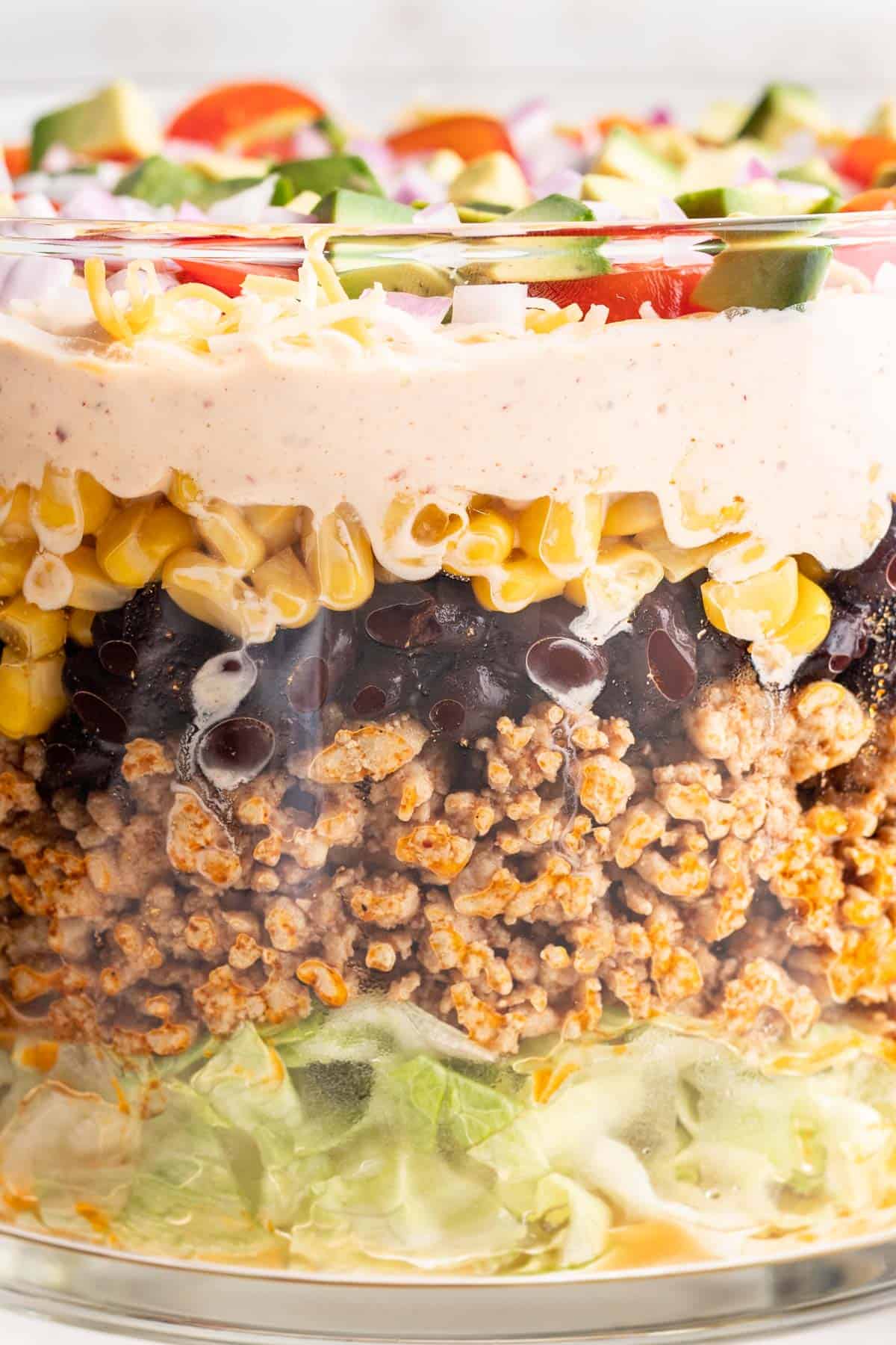 Closeup view of layered taco salad to show the lettuce, ground chicken, black beans, corn, and toppings.