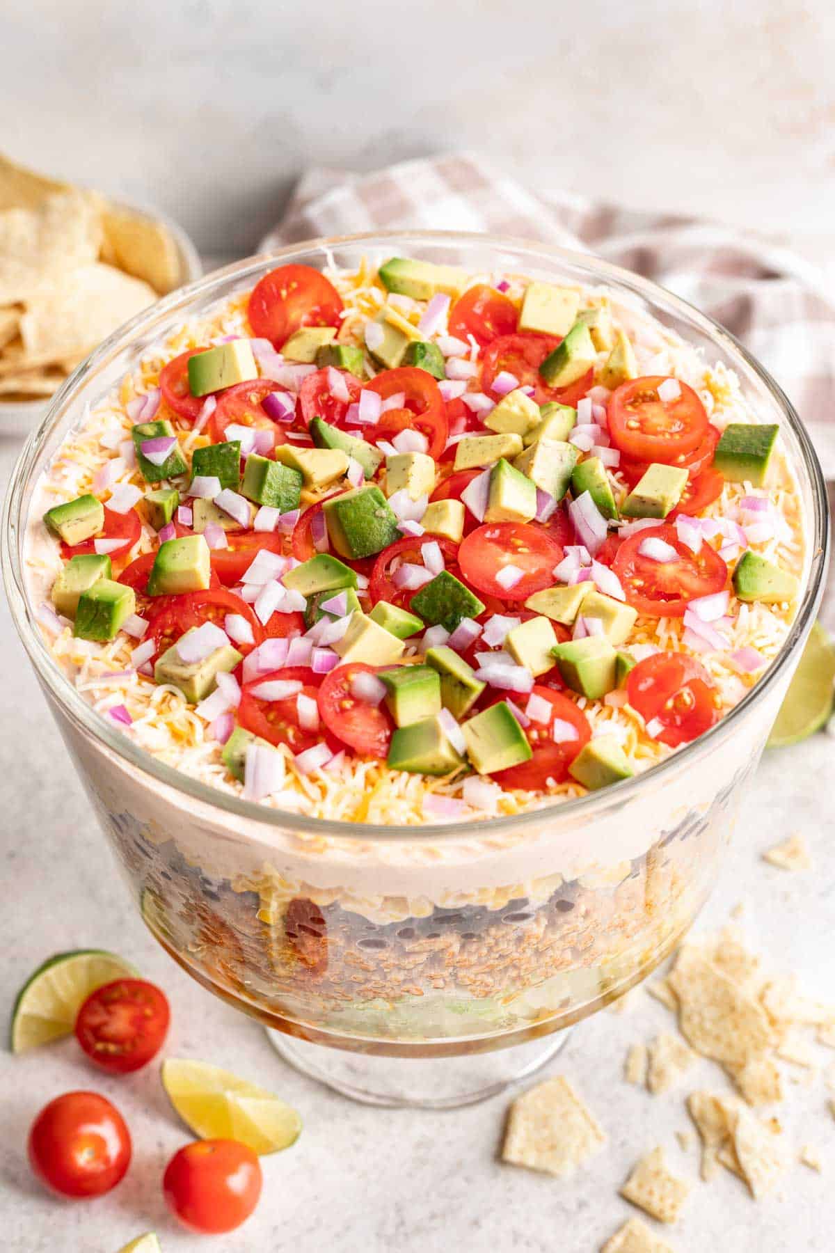 Taco salad layered in a trifle dish with toppings and tortilla chips on the side.