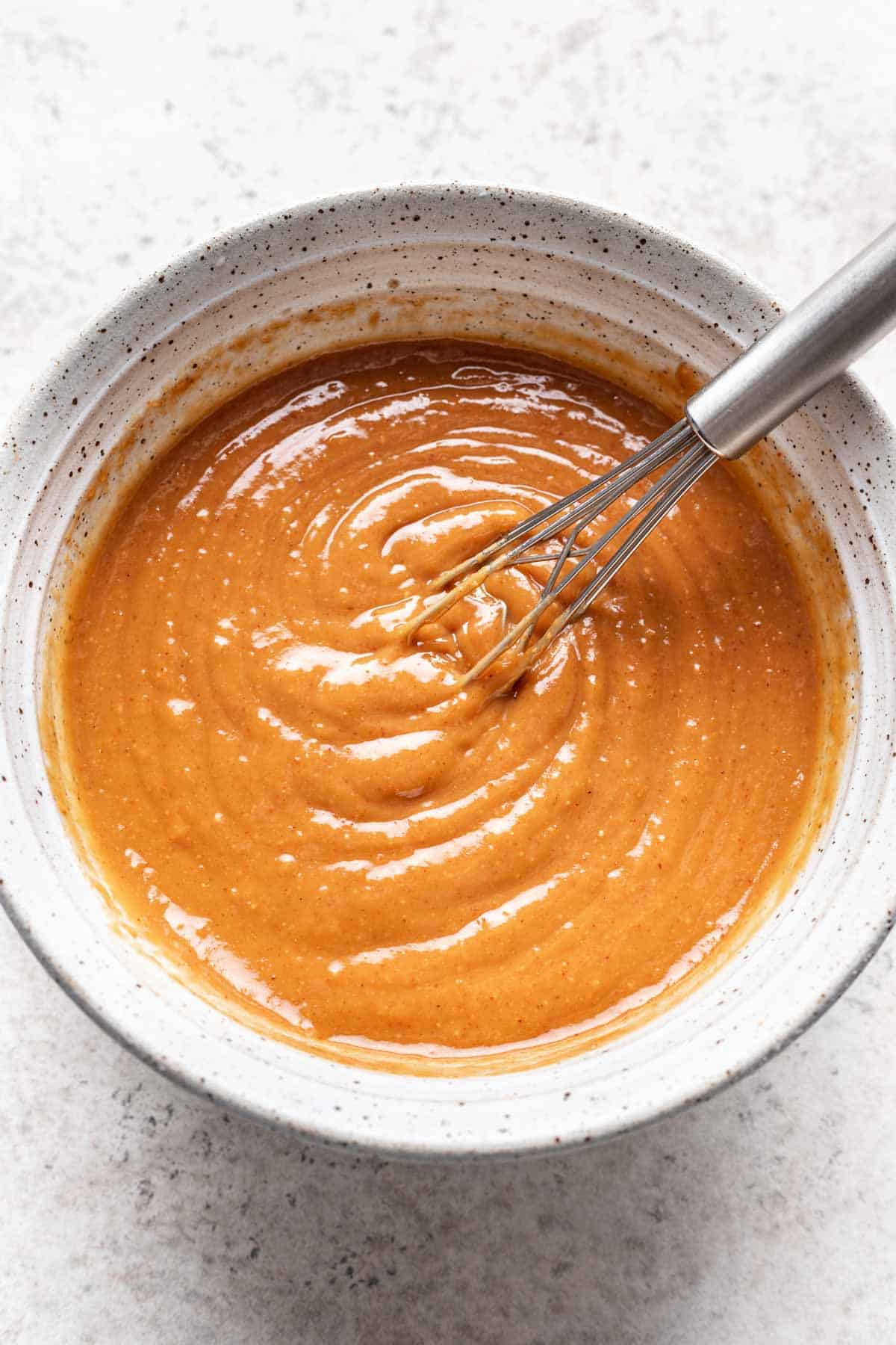 Spicy peanut sauce in a white bowl with a small whisk.