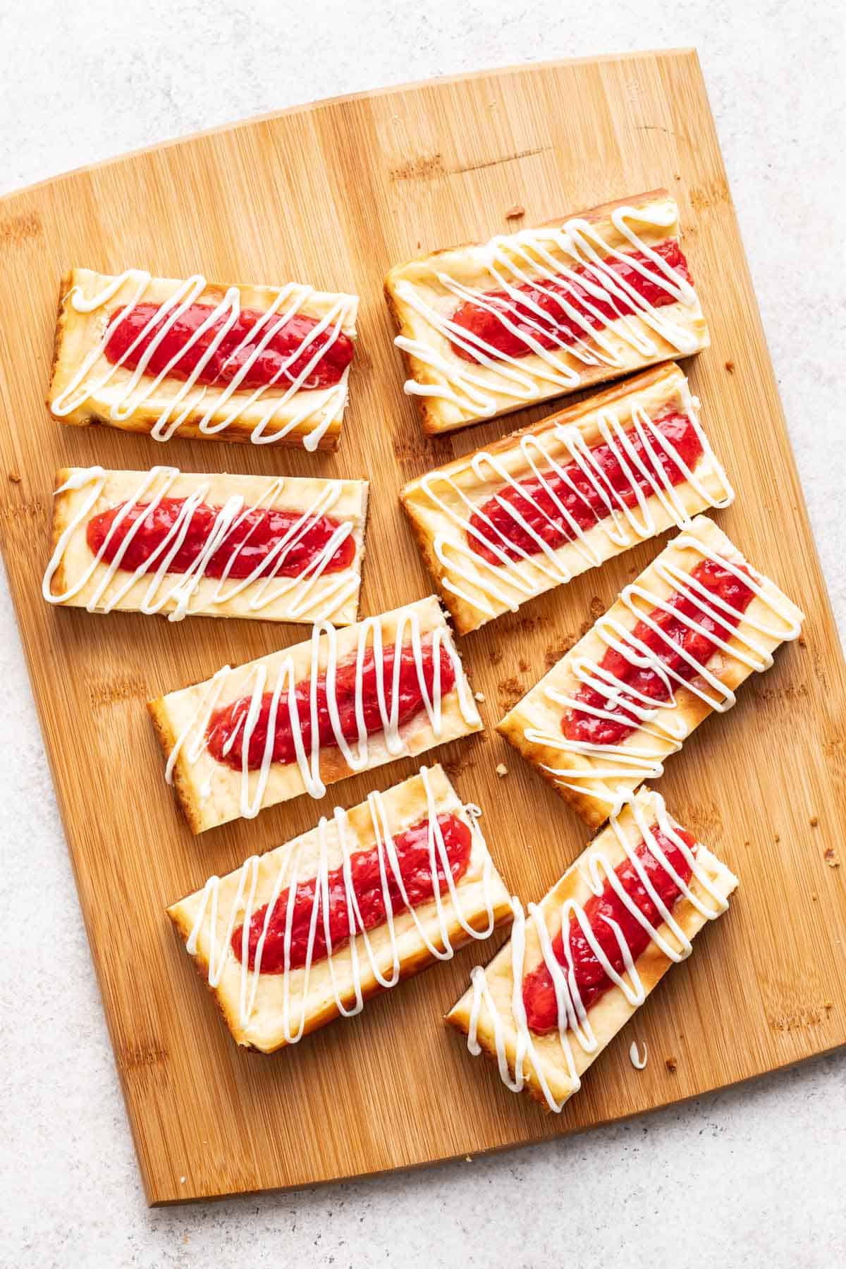 Cheesecake bars with strawberry jam and white chocolate drizzled on top.