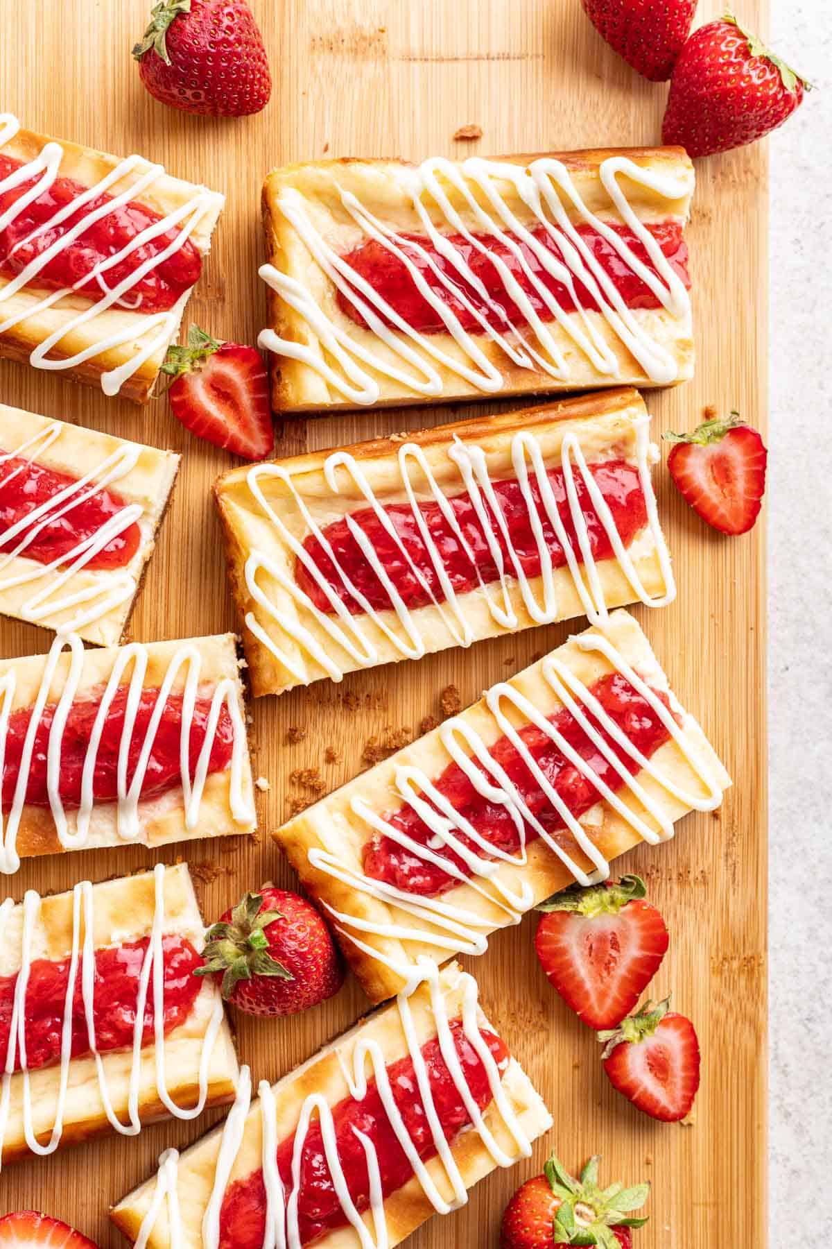 Strawberry Cheesecake Bars on a wood cutting board with strawberries.
