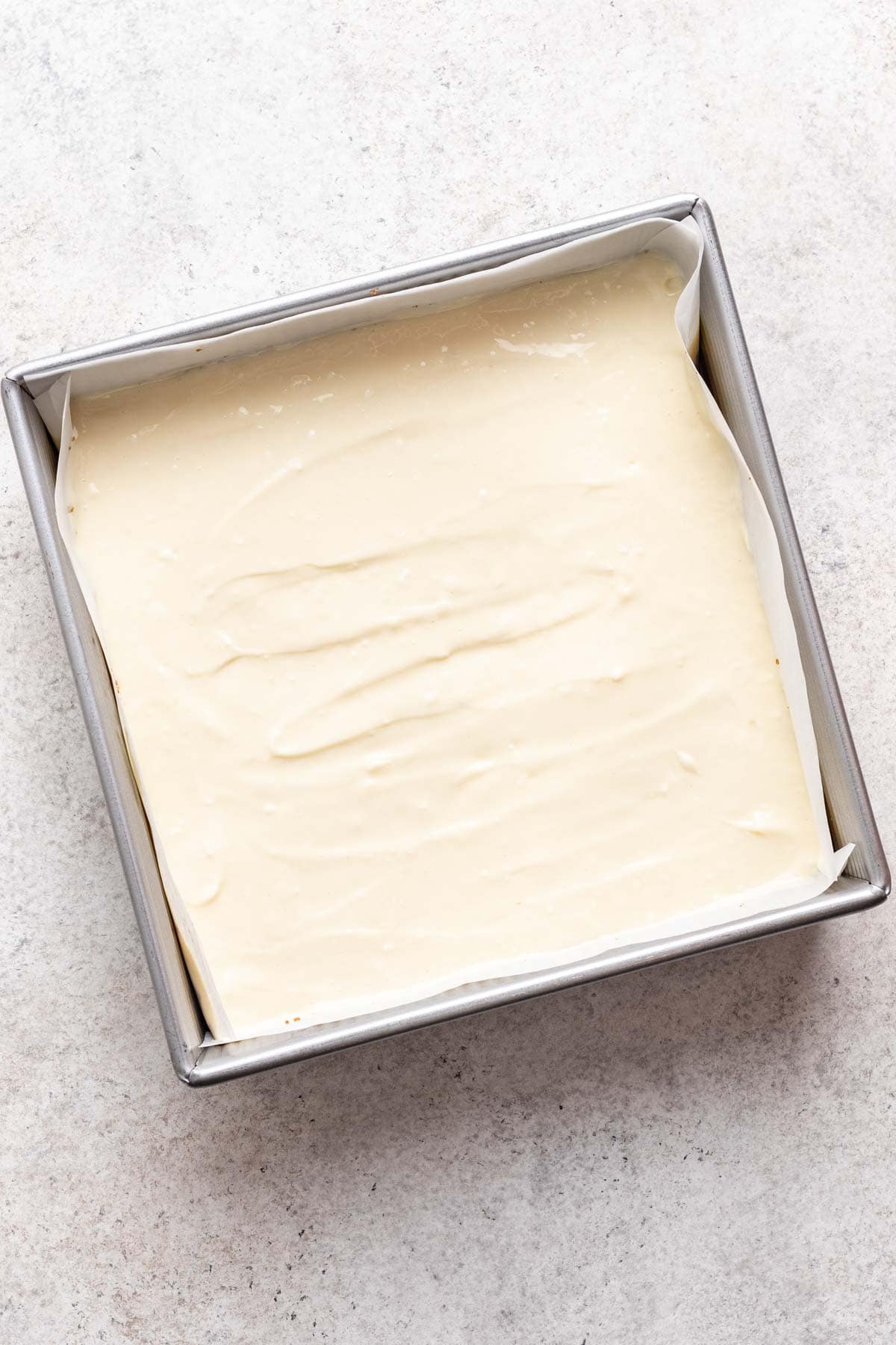 Cheesecake batter added to a 9-inch square baking pan on top of graham cracker crust.