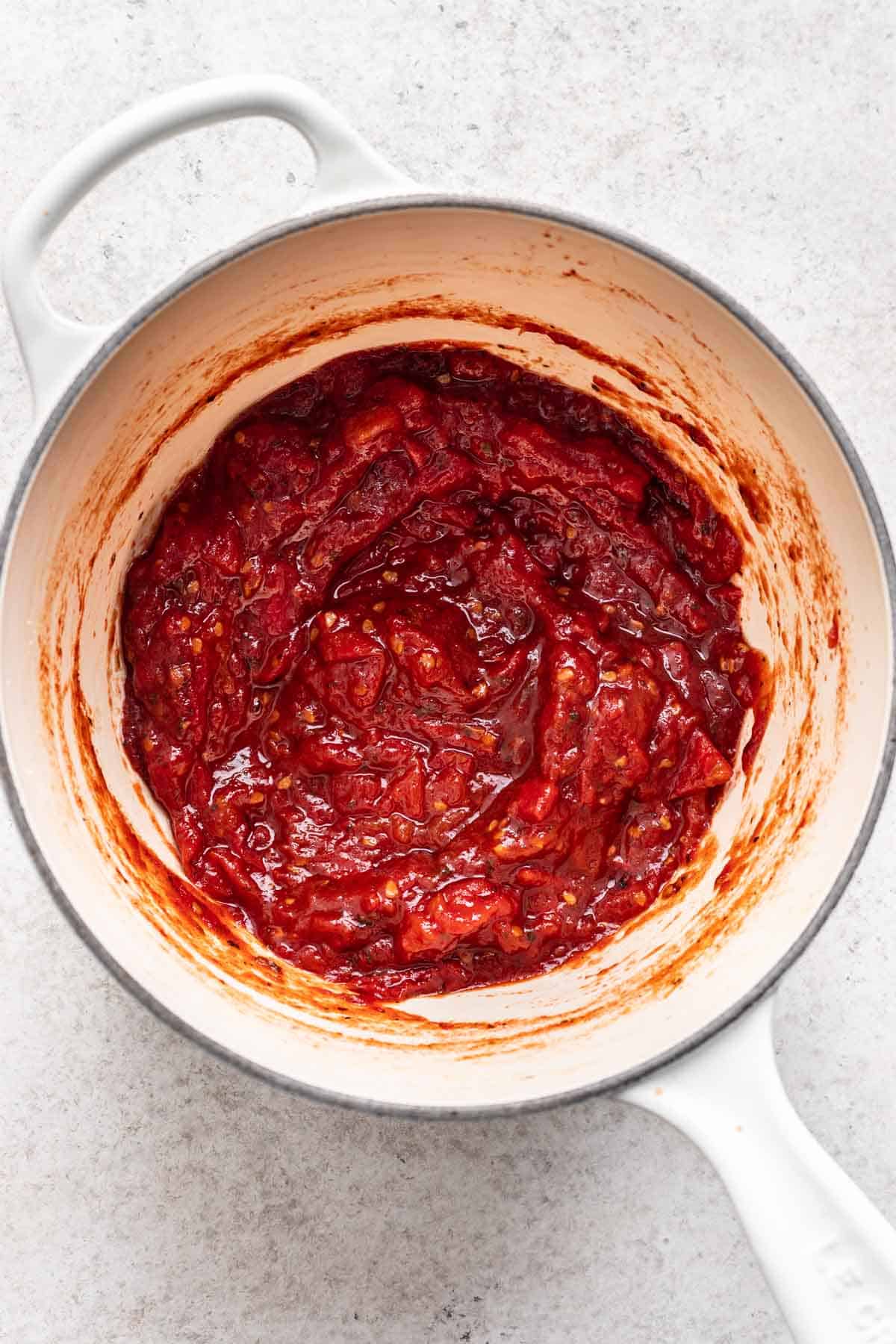 Thick, red tomato jam in a white saucepan.