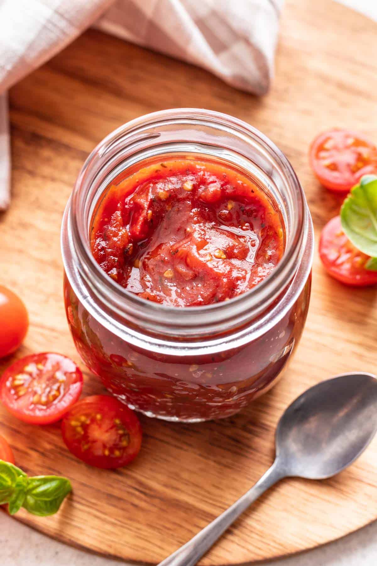 Tomato jam in a jar with fresh tomatoes and basil around it.