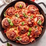 Caprese rolls in a cast iron pan with tomatoes and basil on top.