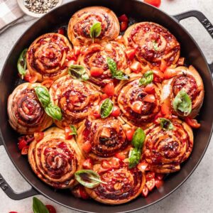 Caprese rolls in a cast iron pan with tomatoes and basil on top.