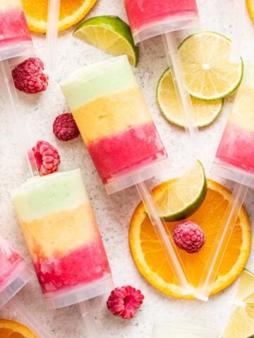 Homemade push up popsicles with raspberry, mango, and lime sherbet ice cream inside.