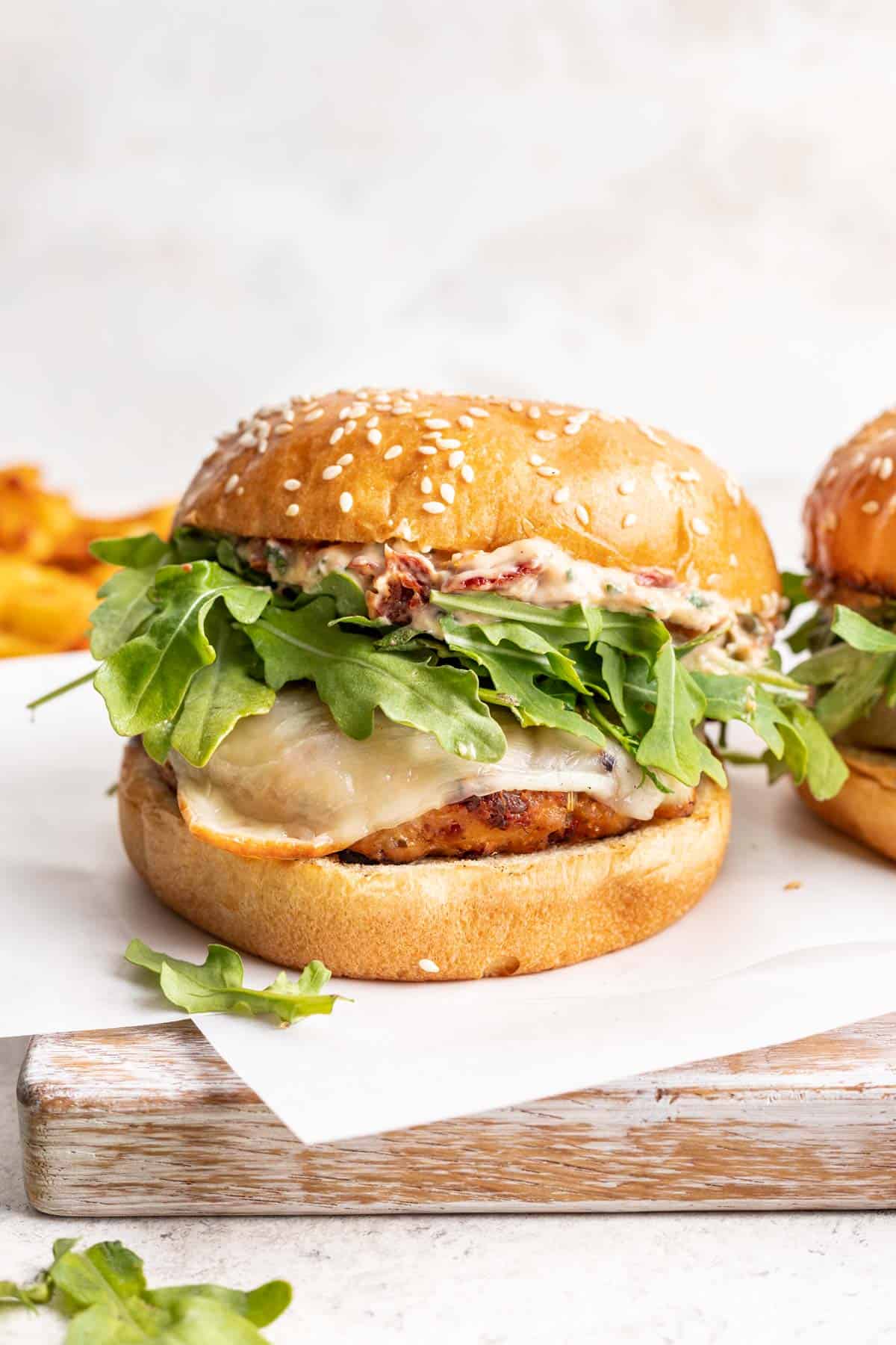 Marry Me Chicken Burger with aioli, cheese, and arugula on a hamburger bun.
