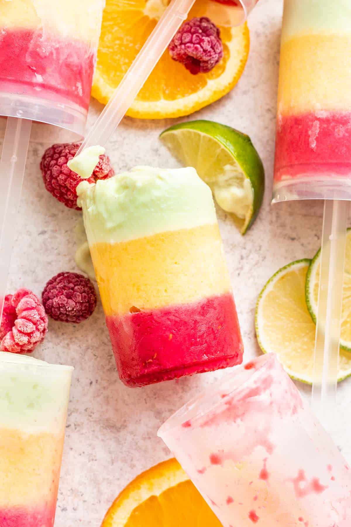 A push up popsicle popped outside its mold to show the raspberry, mango, and lime homemade sherbet.