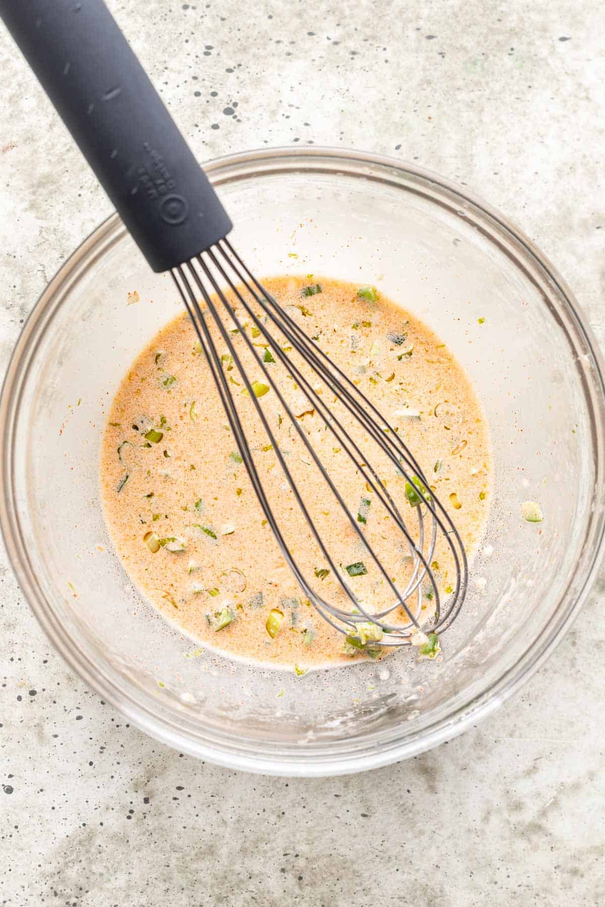 Sauce for street corn salsa in a bowl with a whisk.