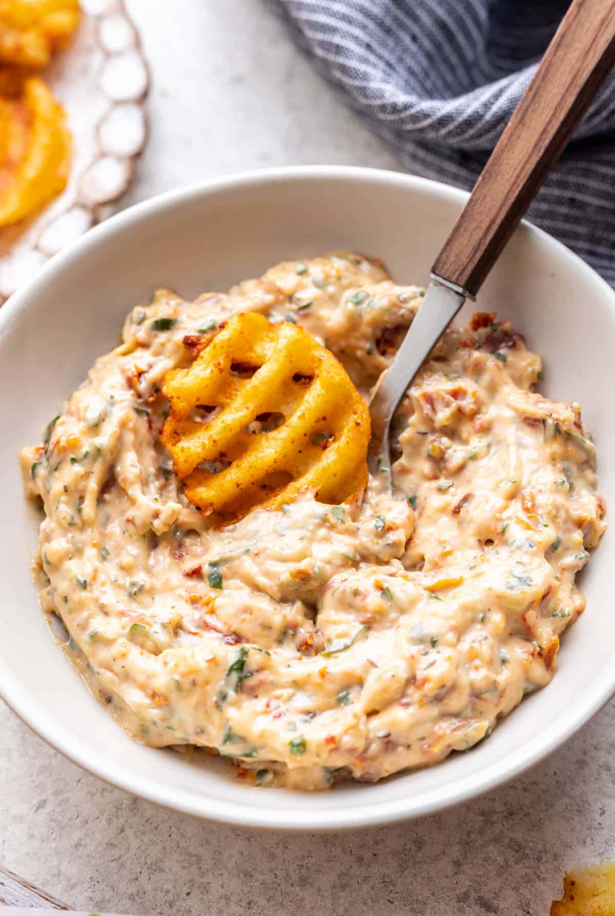 Sun dried tomato aioli in a bowl with a waffle fry dipped into it.