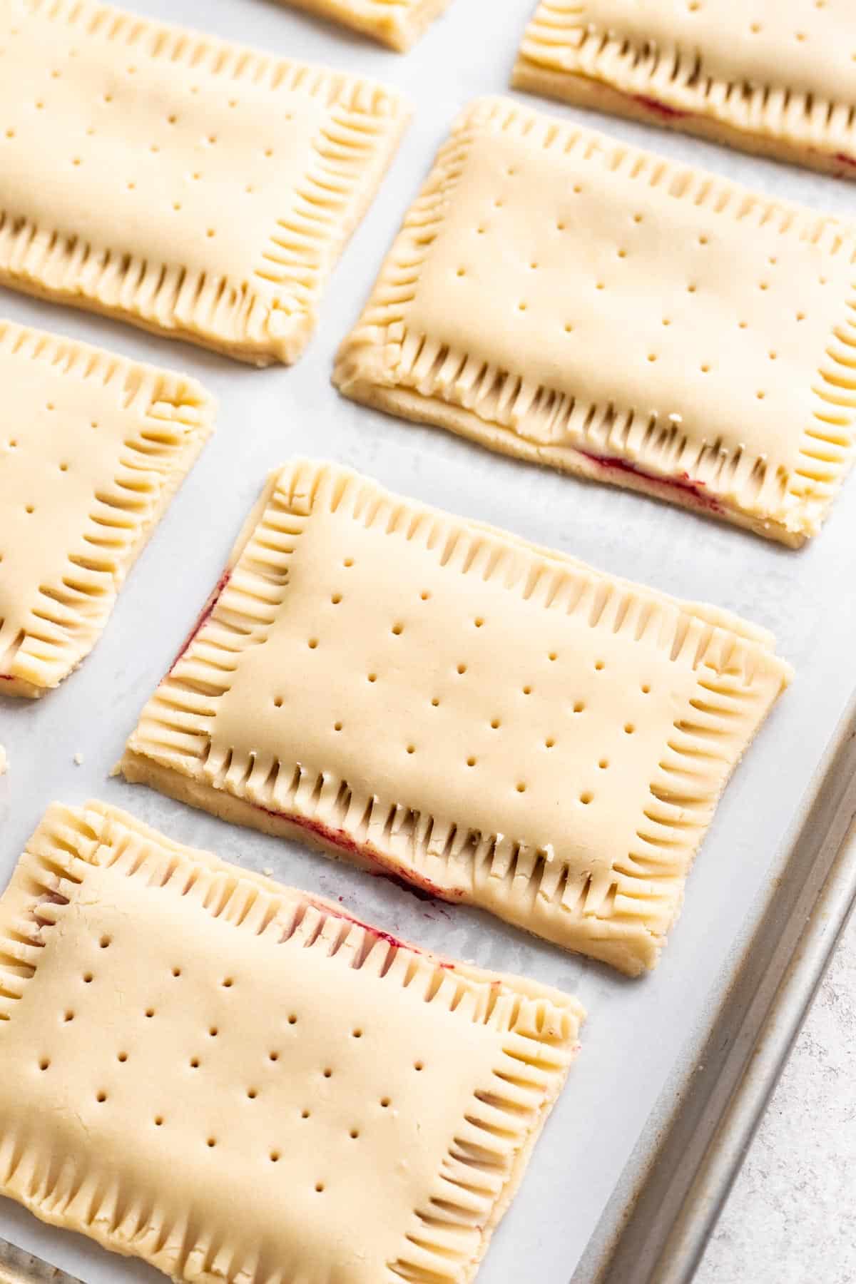 Pop tarts on a baking sheet before baking, with crimped edges and holes poked on top.
