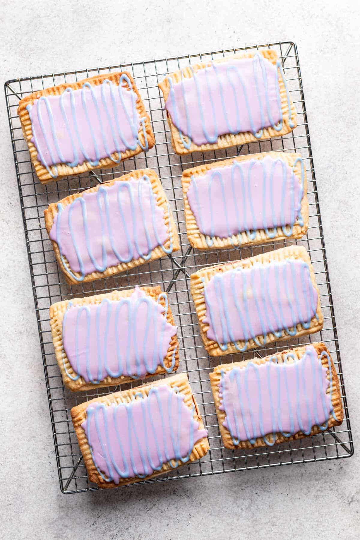 Pop tarts with purple glaze and blue glaze drizzle over top on a cooling rack.