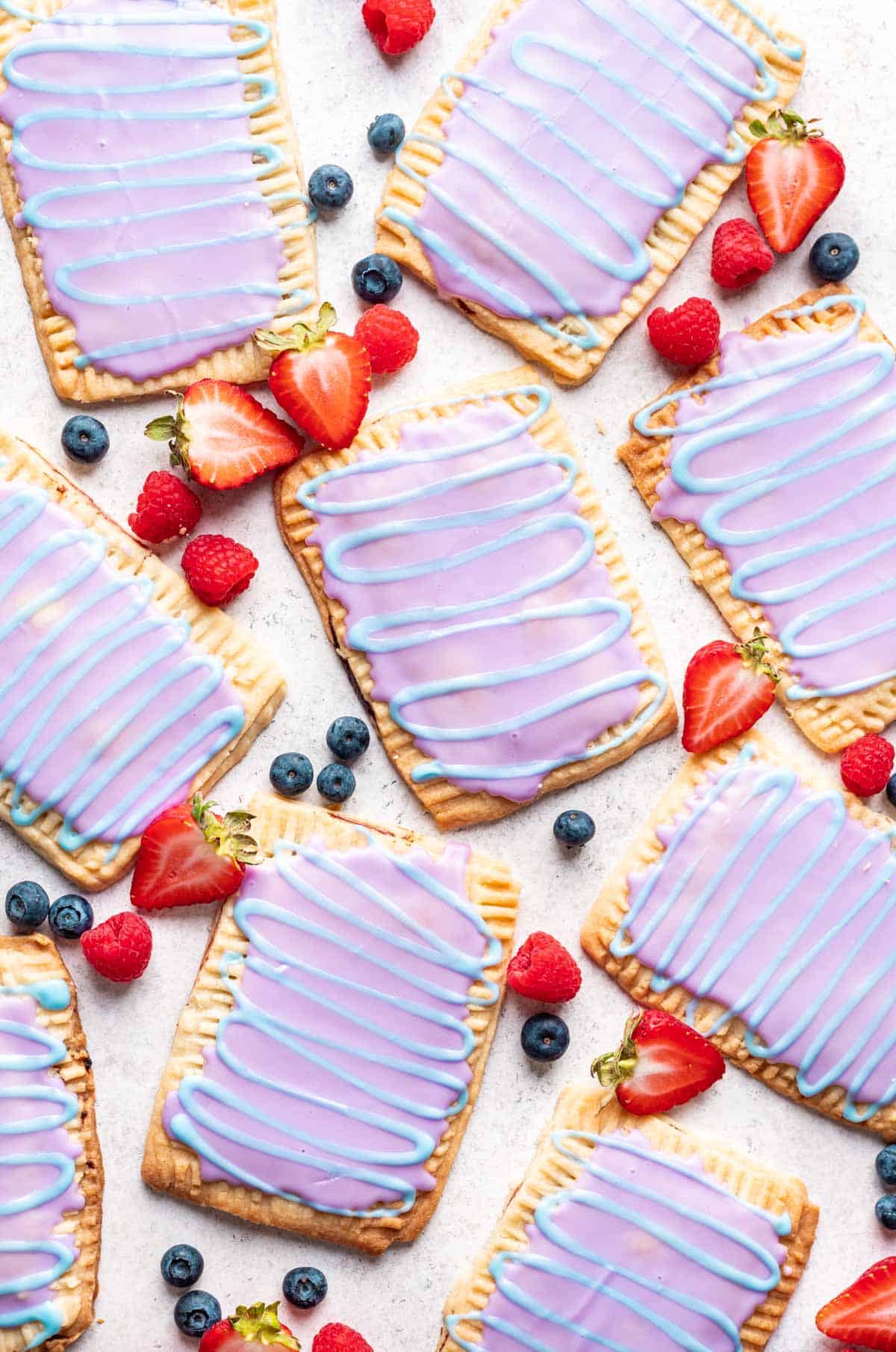 Homemade wild berry pop tarts on a white background with fresh berries around them.