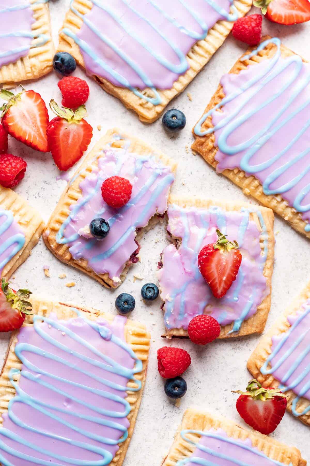 A broken wild berry pop tart surrounded by other pop tarts and fresh berries.