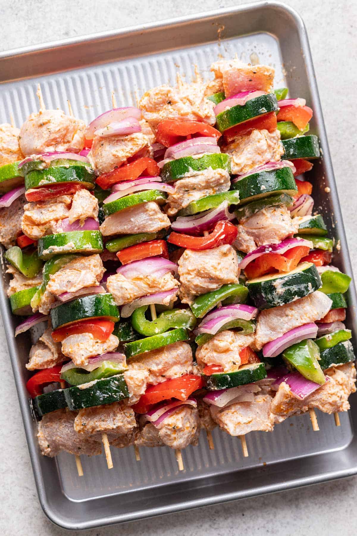 Raw yogurt marinated chicken skewers on a tray just before grilling.