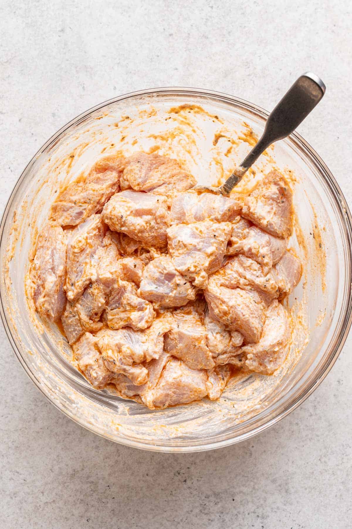 Cubed chicken marinating in a bowl with greek yogurt and seasonings.