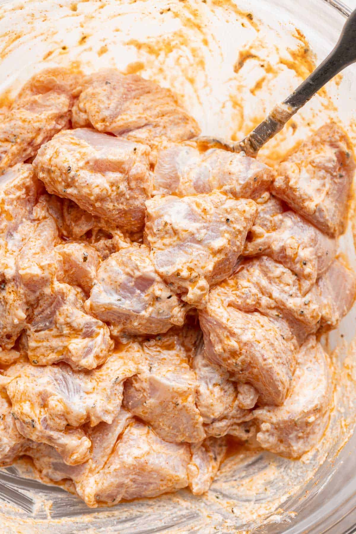 Yogurt marinated chicken in a bowl with seasonings.