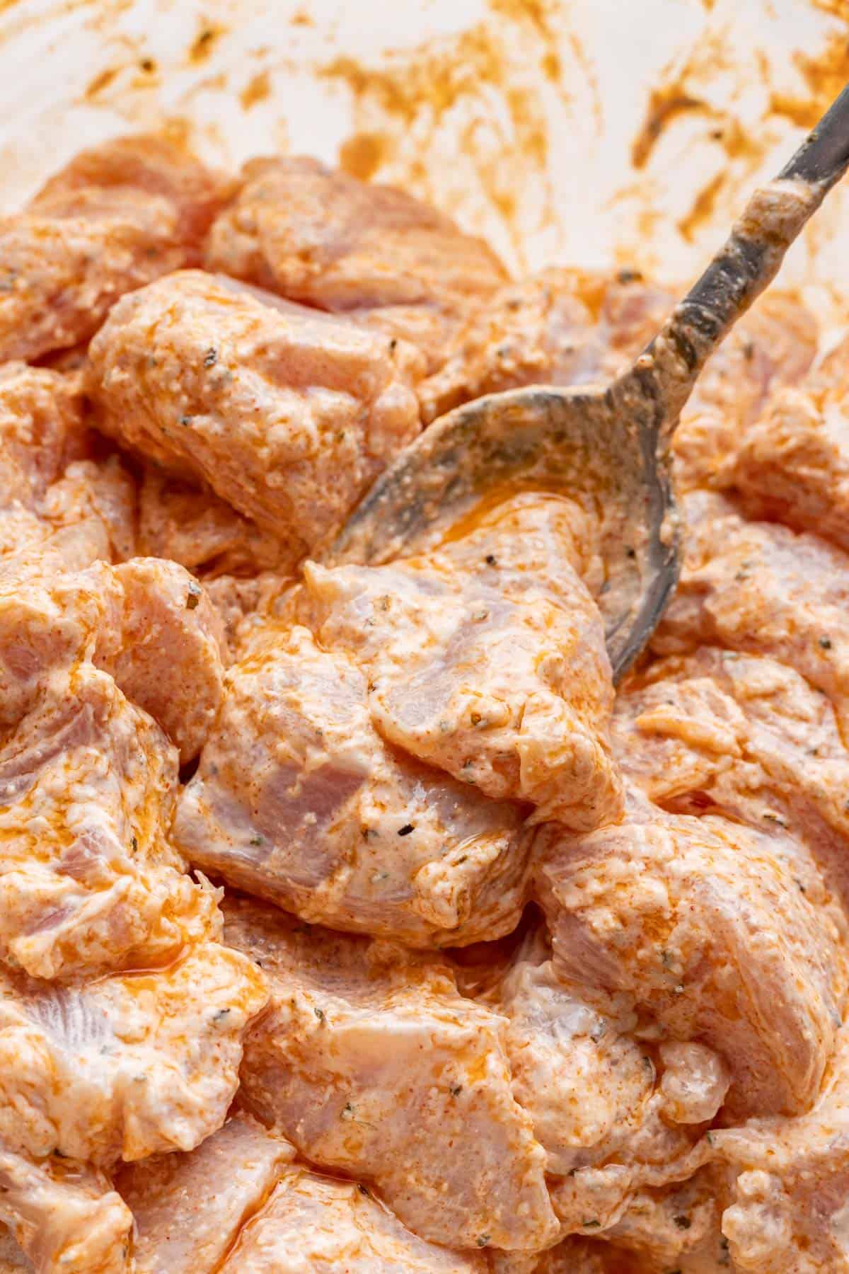 Cubed chicken marinated in yogurt and seasoning with a spoon.
