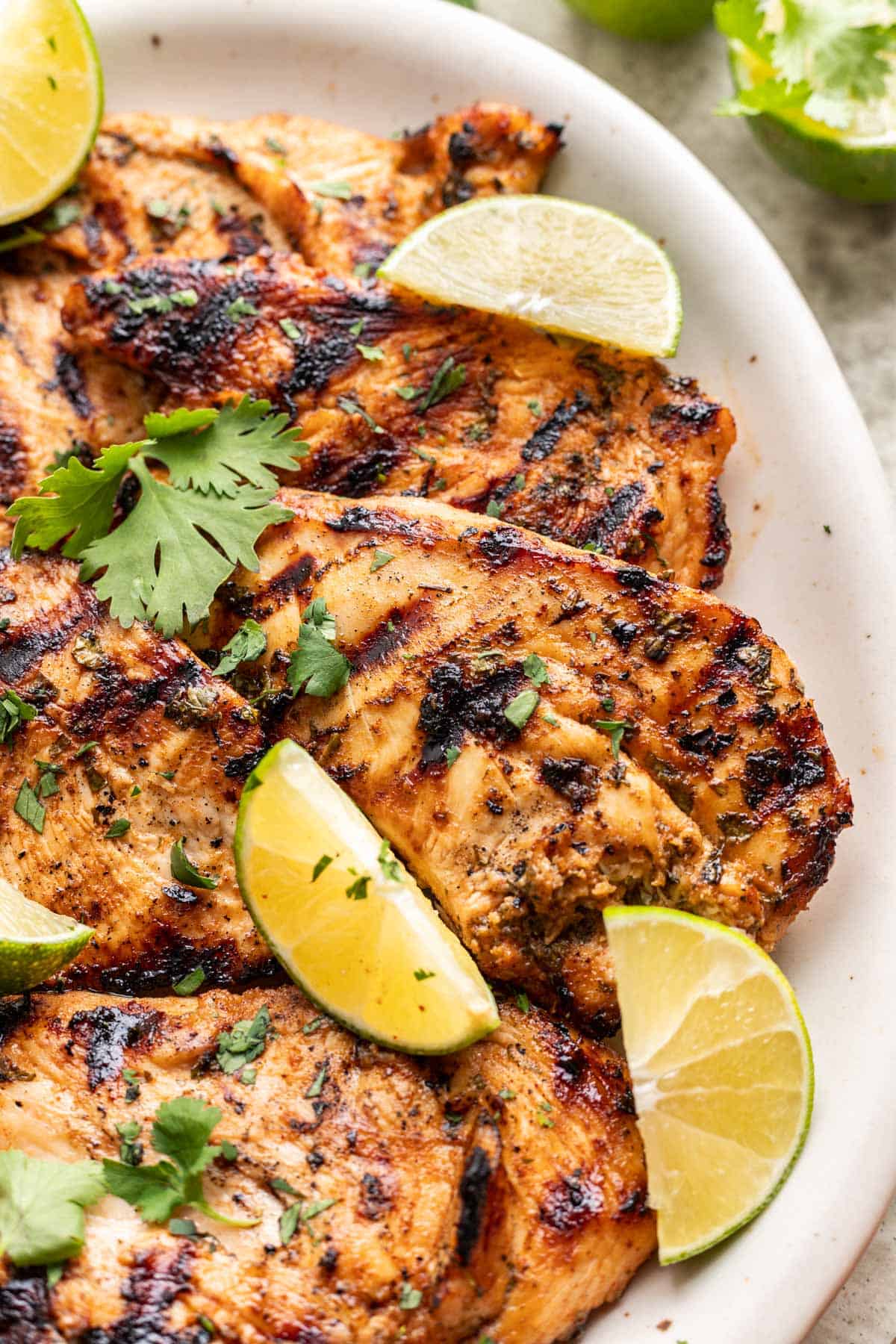 Grilled cilantro lime chicken with fresh cilantro and limes on top of it.