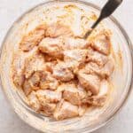 Chicken marinating in yogurt in a glass bowl.