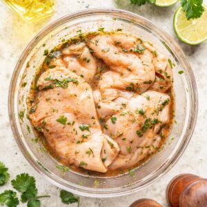 Raw chicken in a bowl with cilantro lime marinade.