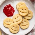 Smiley potatoes on a white plate with ketchup on the side.