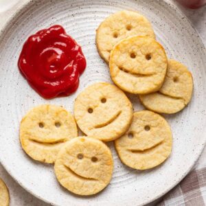 Smiley potatoes on a white plate with ketchup on the side.