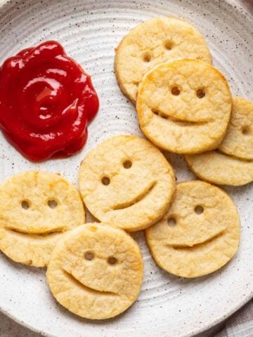 Smiley potatoes on a white plate with ketchup on the side.