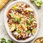 Street corn grilled chicken on a serving platter with limes and cilantro.
