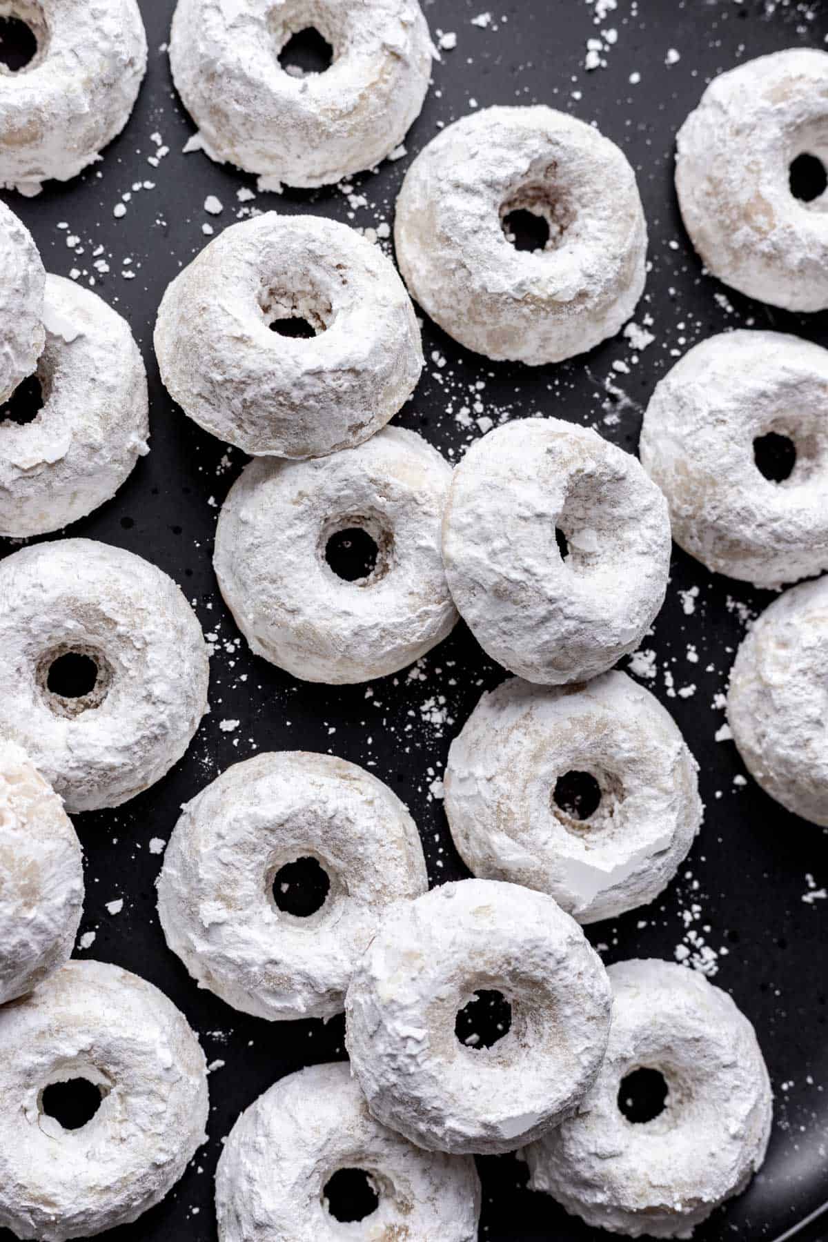 Mini powdered donuts stacked on one another on a black dish.