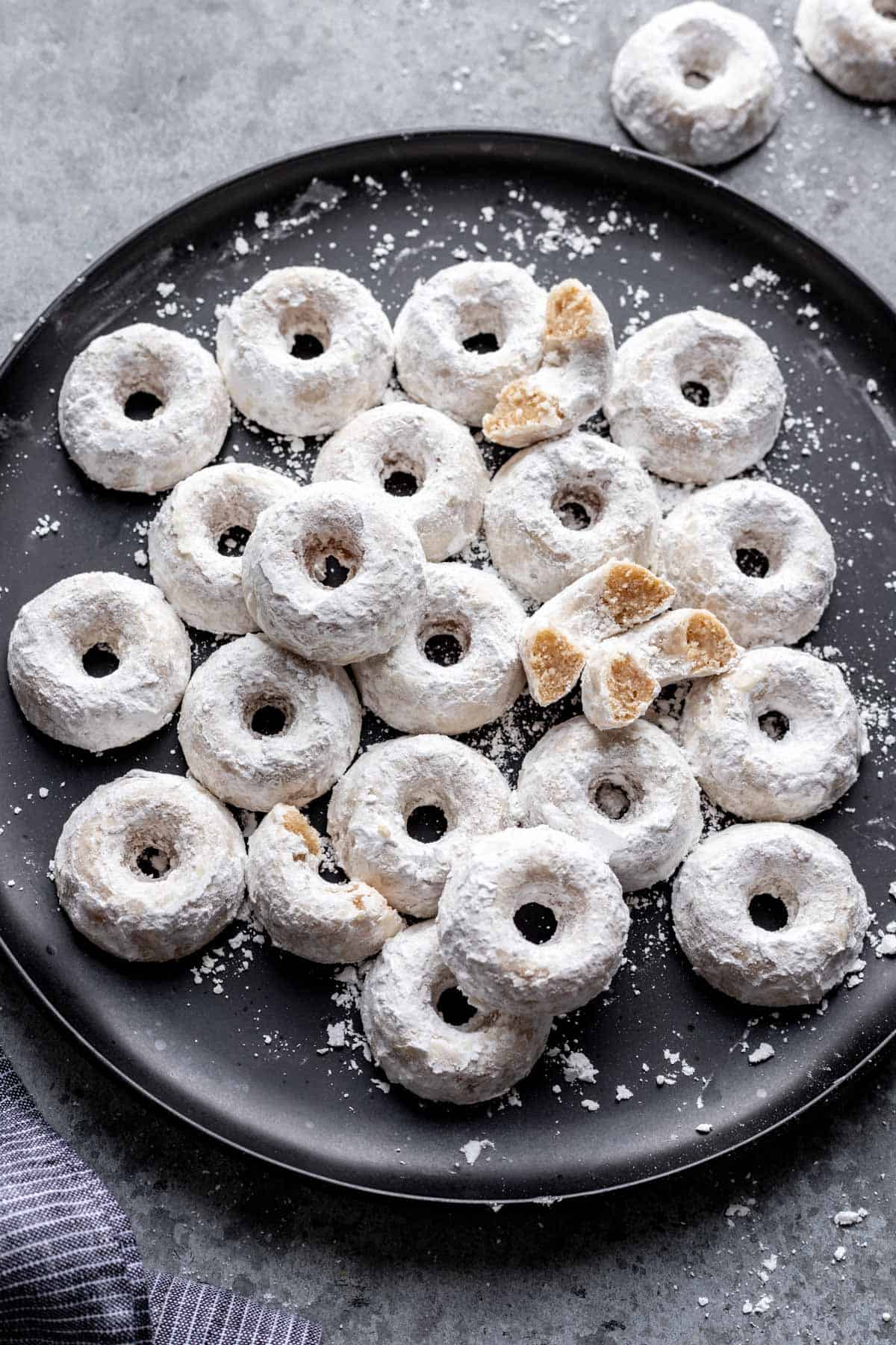 Mini powdered donuts on a black serving plate.