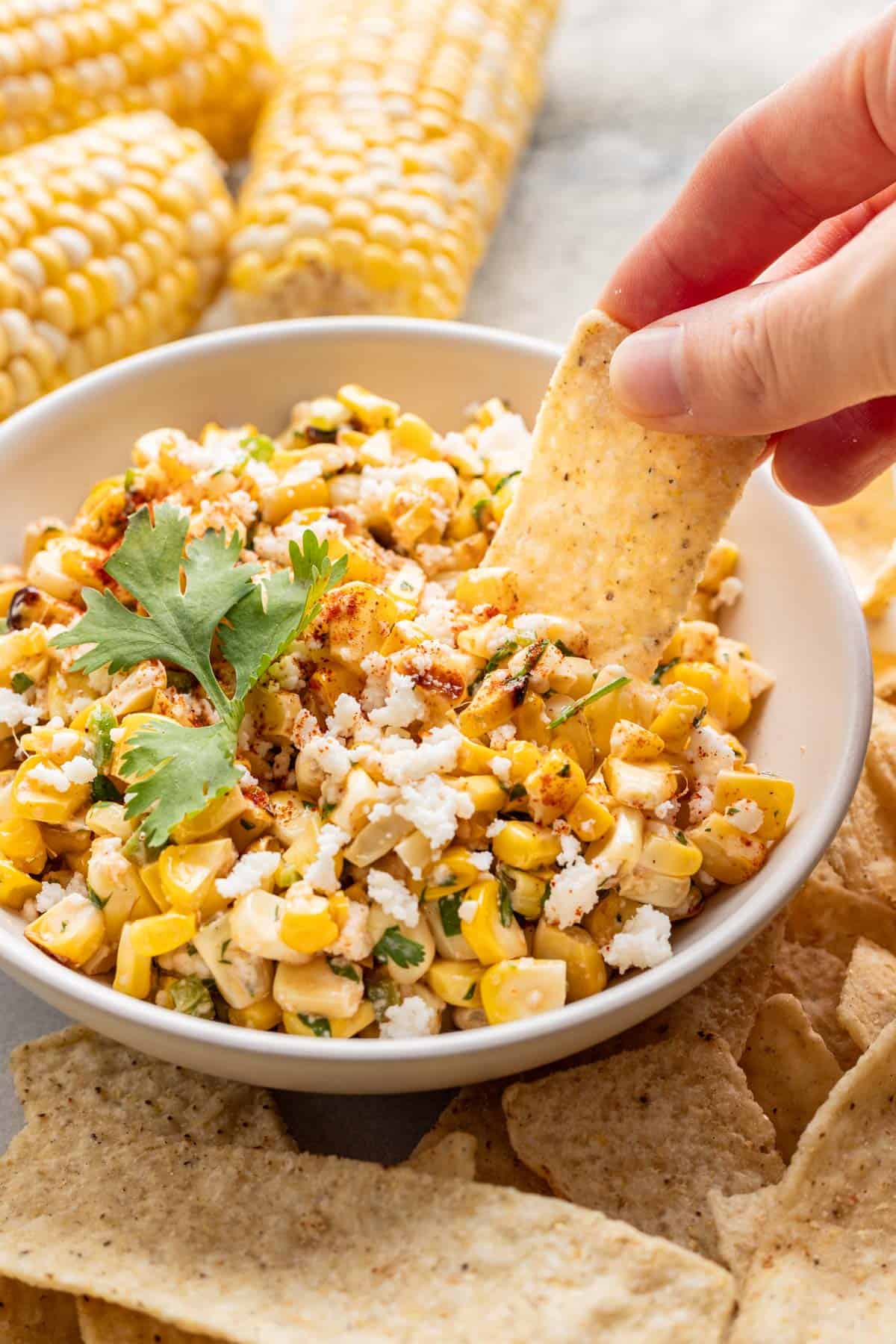 A hand dipping a tortilla chip in street corn salsa.
