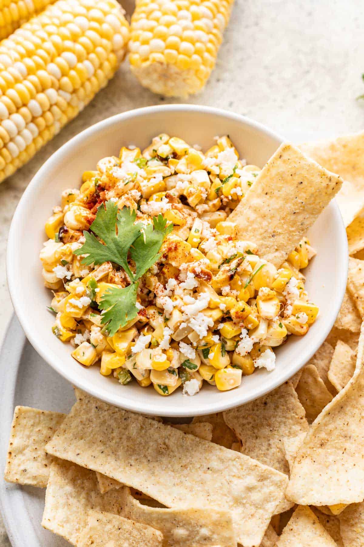 Street corn salsa in a bowl with a tortilla chip for dipping.
