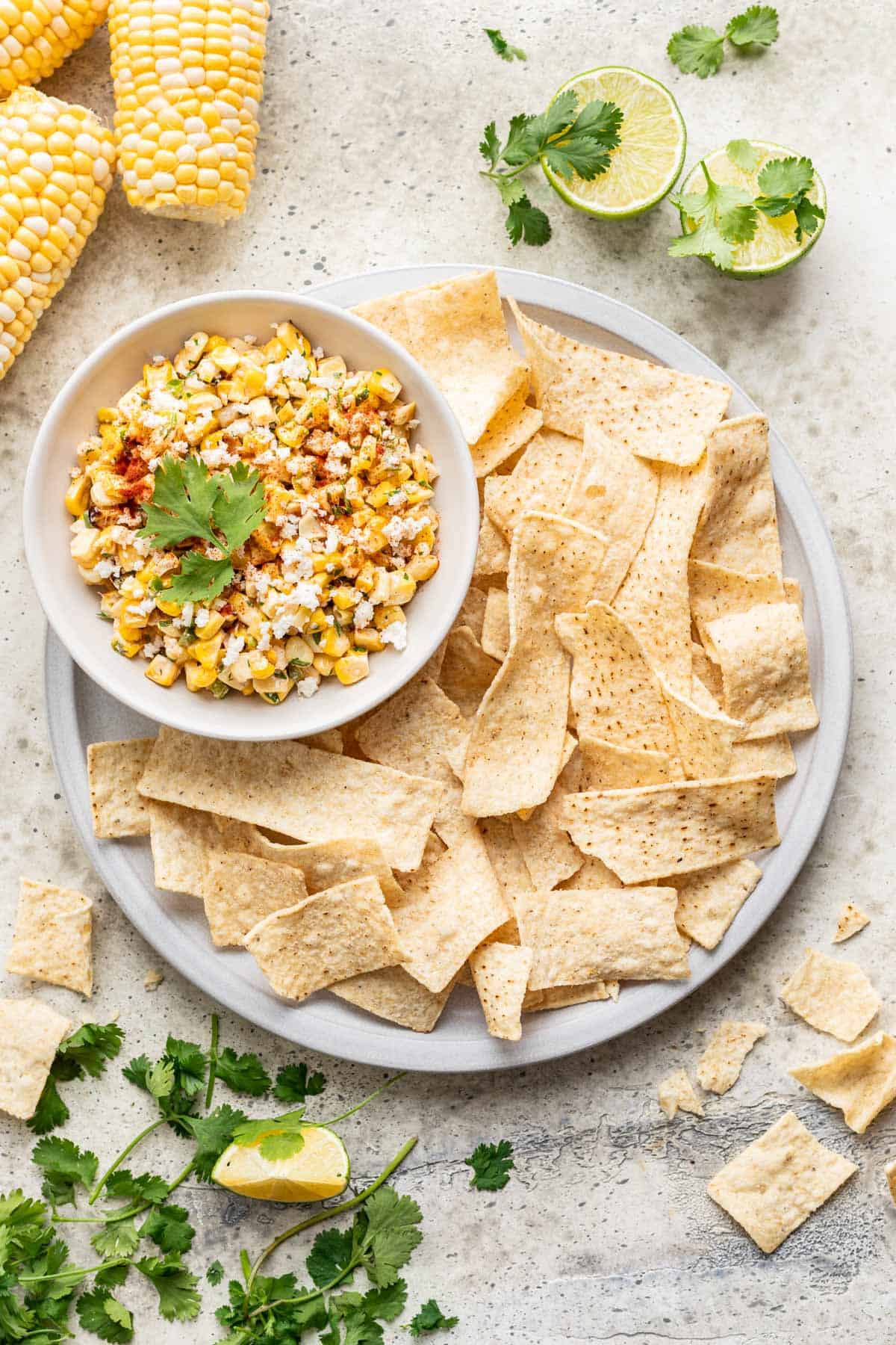 Street corn salsa in a serving bowl with a plate of tortilla chips for scooping.